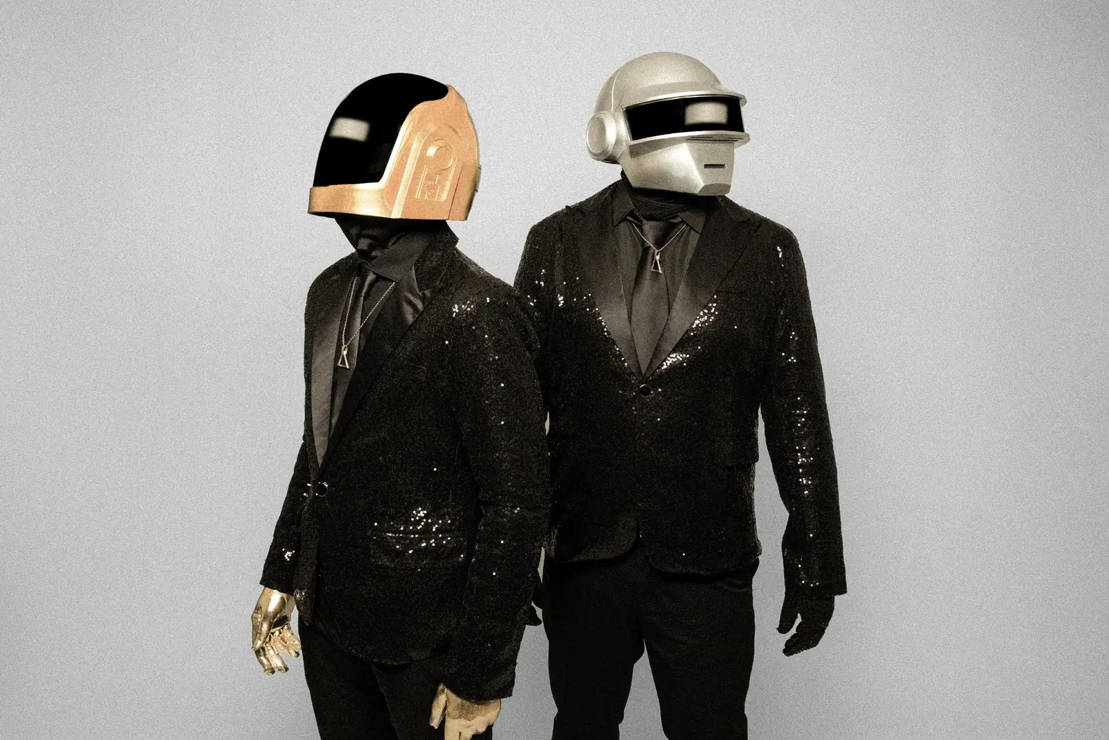 The two performers on a grey backdrop, one wearing gold gloves